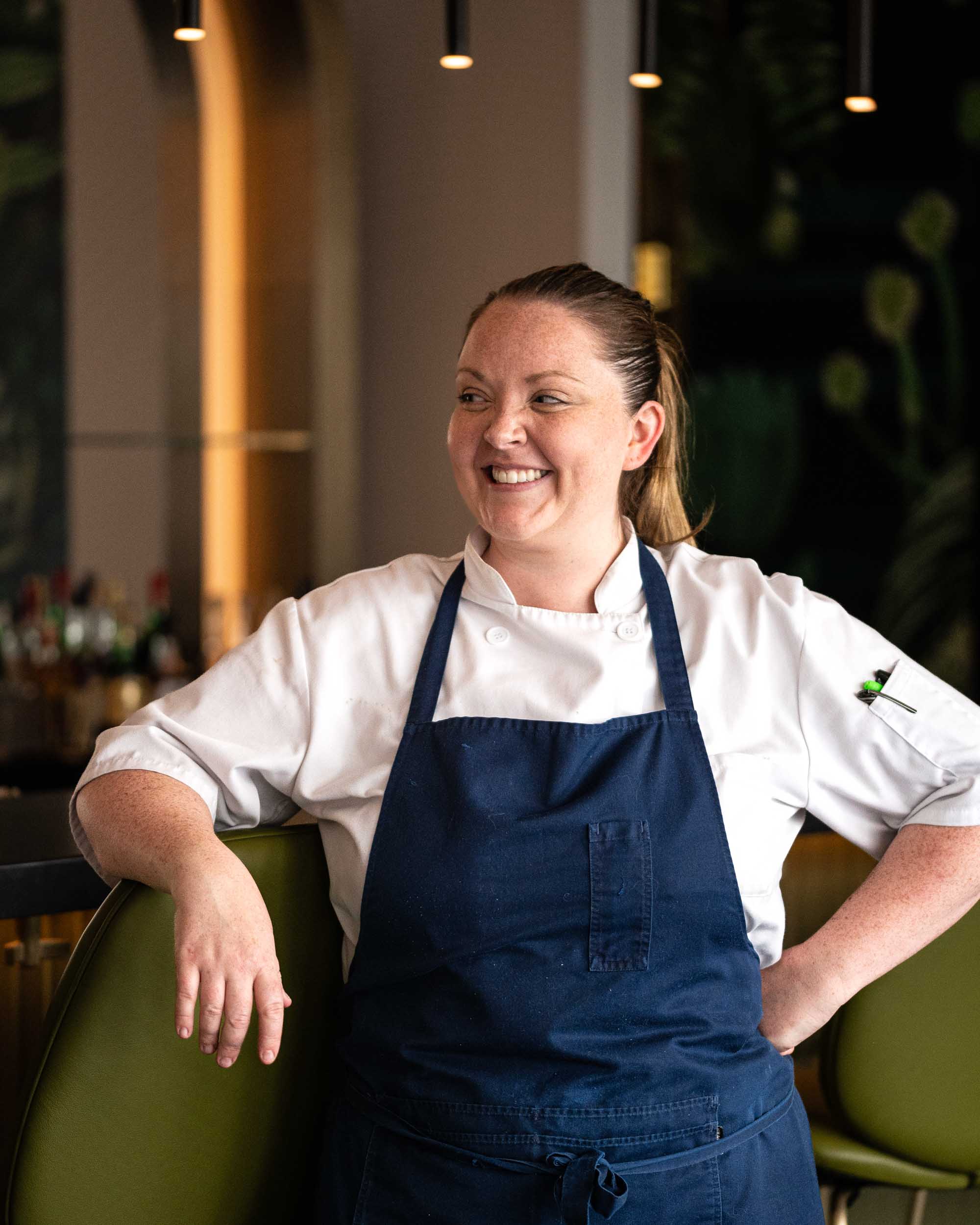 Chef Moira Murray smiles and leans on a green chair at Peacock Wine Bar Halifax