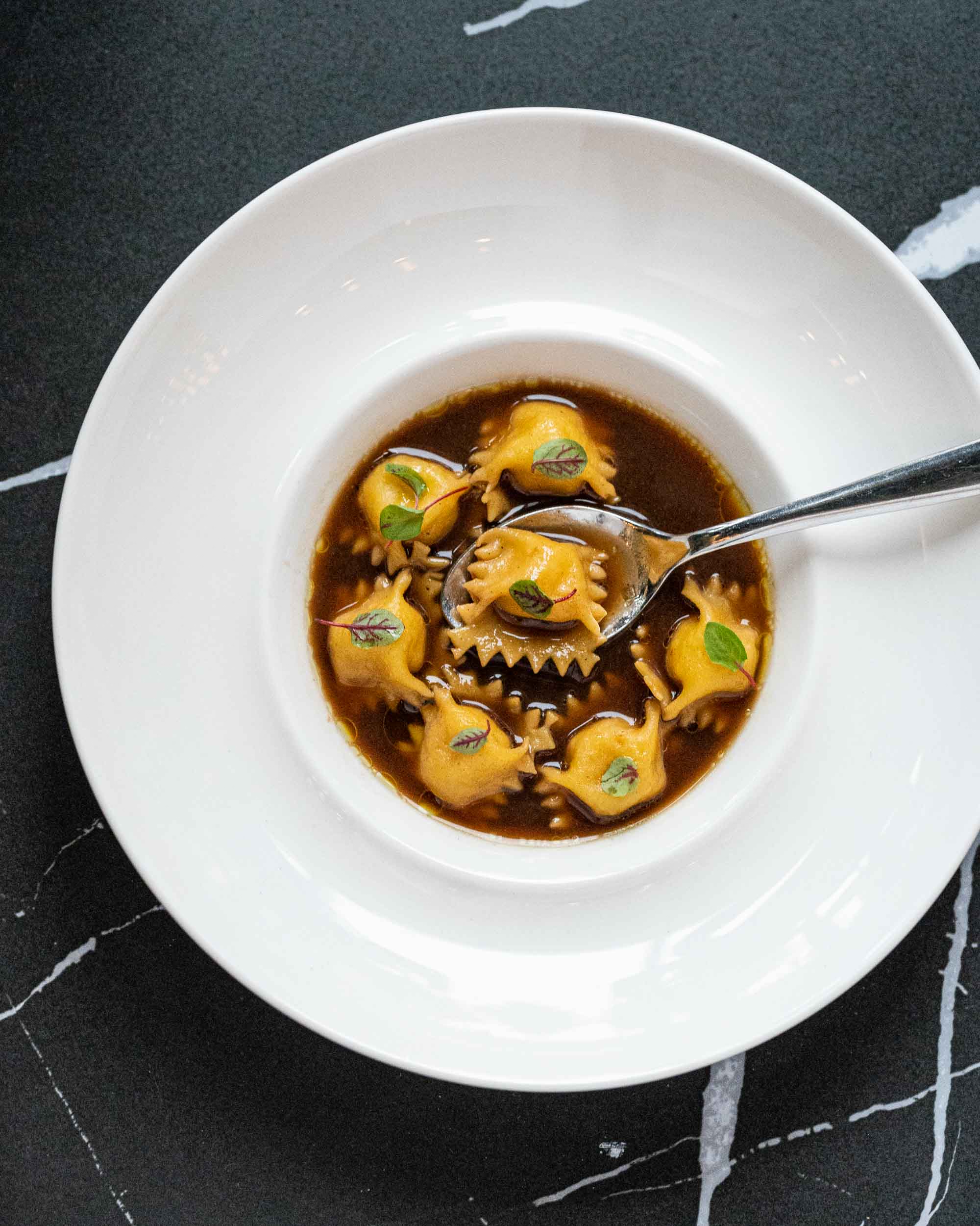 An overhead view of potato and parmesan agnolotti and smoked potato brodo in a white bowl