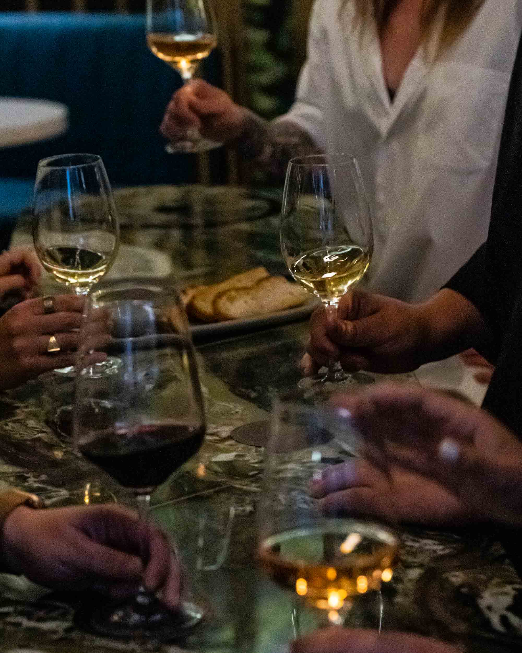 Guests at a dark stone table hold glasses of white and red wine